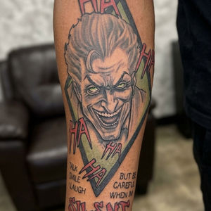 Joker portrait tattoo with HA HA text on a forearm.