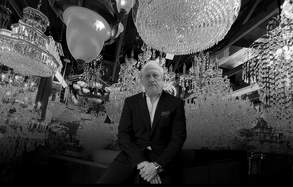 A picture of Pierre Kattan sitting in Pierre Lighting showroom located in Davie Florida. In the background crystal chandelier