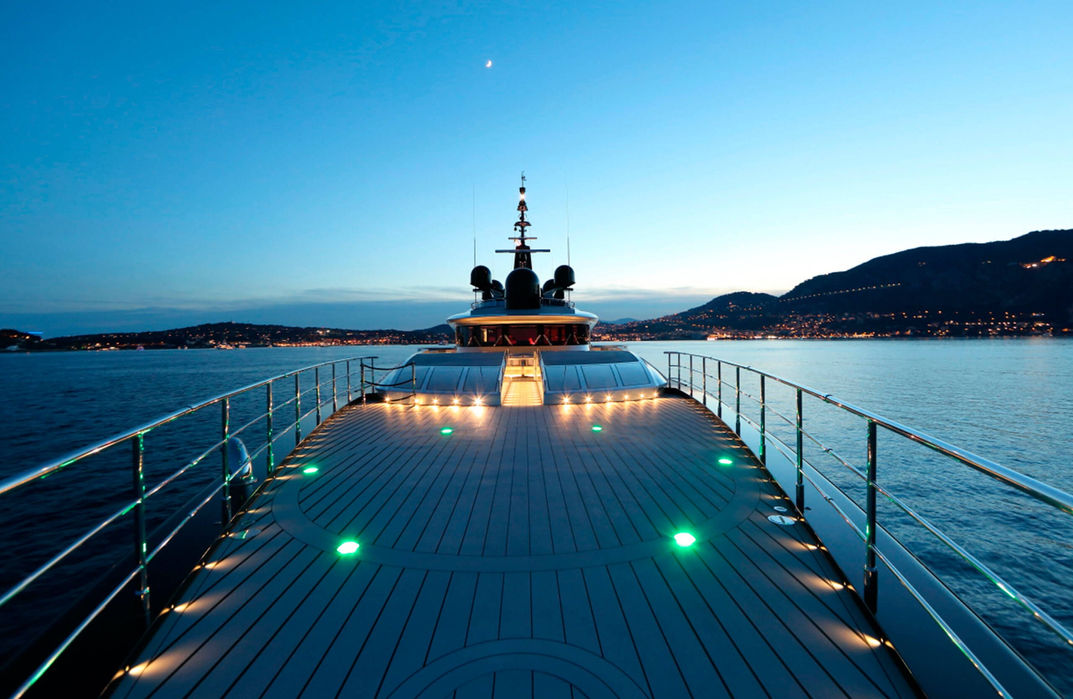 Okto superyacht cruising at night with a lit bow walkway.