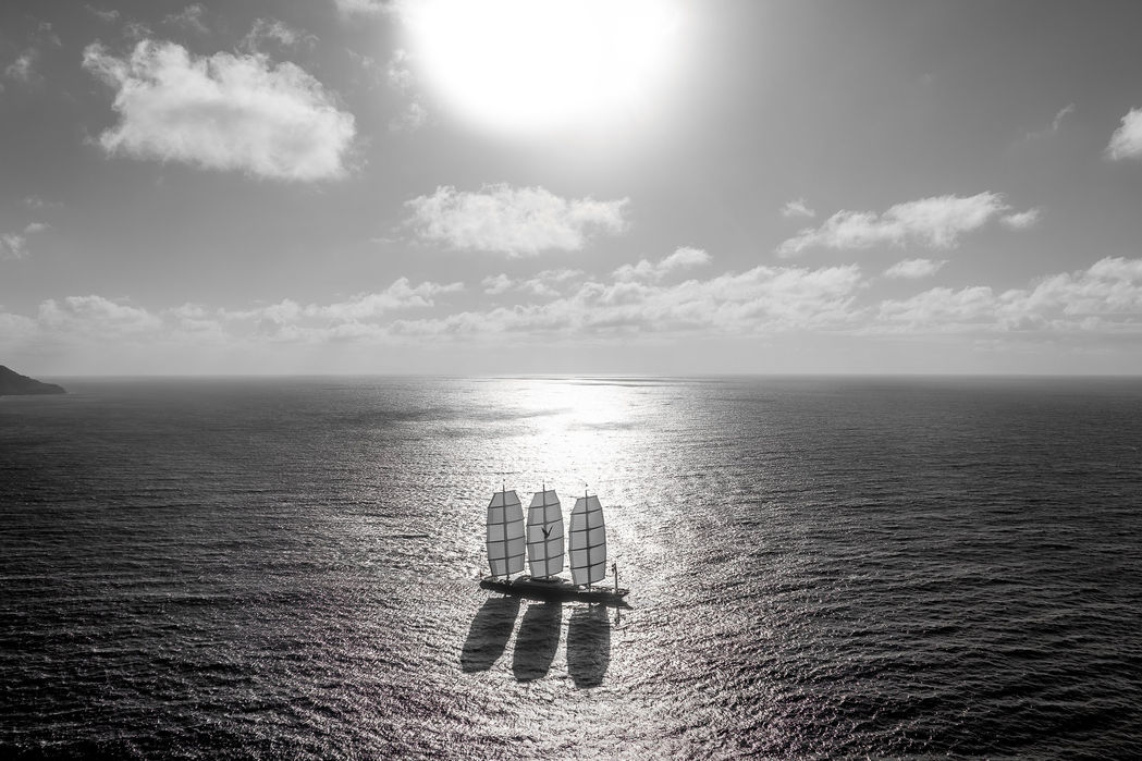 Dramatic silhouette of a sailing superyacht at sea during sunset.