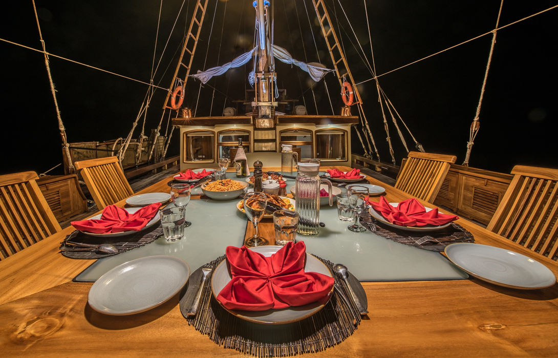 Evening outdoor dining setup onboard Carpe Diem Phinisi during a private Komodo yacht charter with Navélia Yacht Charters Indonesia.