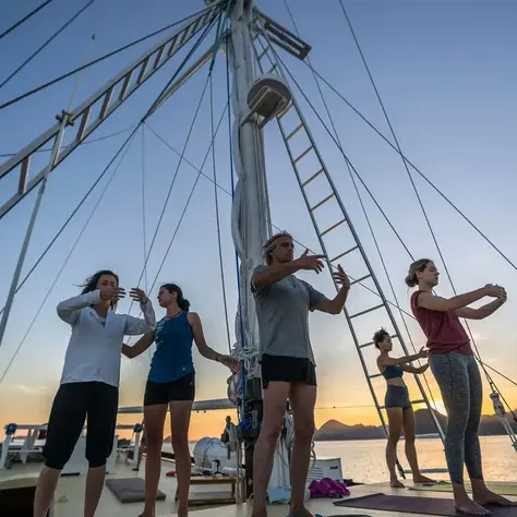 Guests practicing sunrise yoga on the deck of a luxury yacht in Indonesia, with calm water and soft morning light creating a wellness-focused atmosphere.