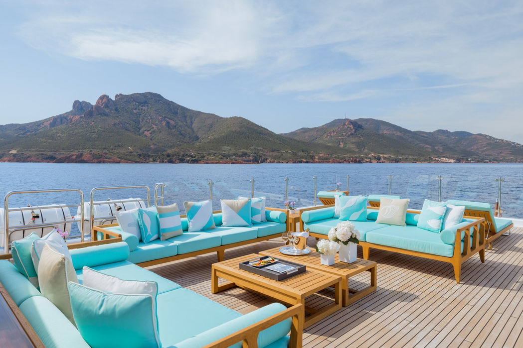 Outdoor lounge setup on Clelia III with turquoise cushions and sea backdrop