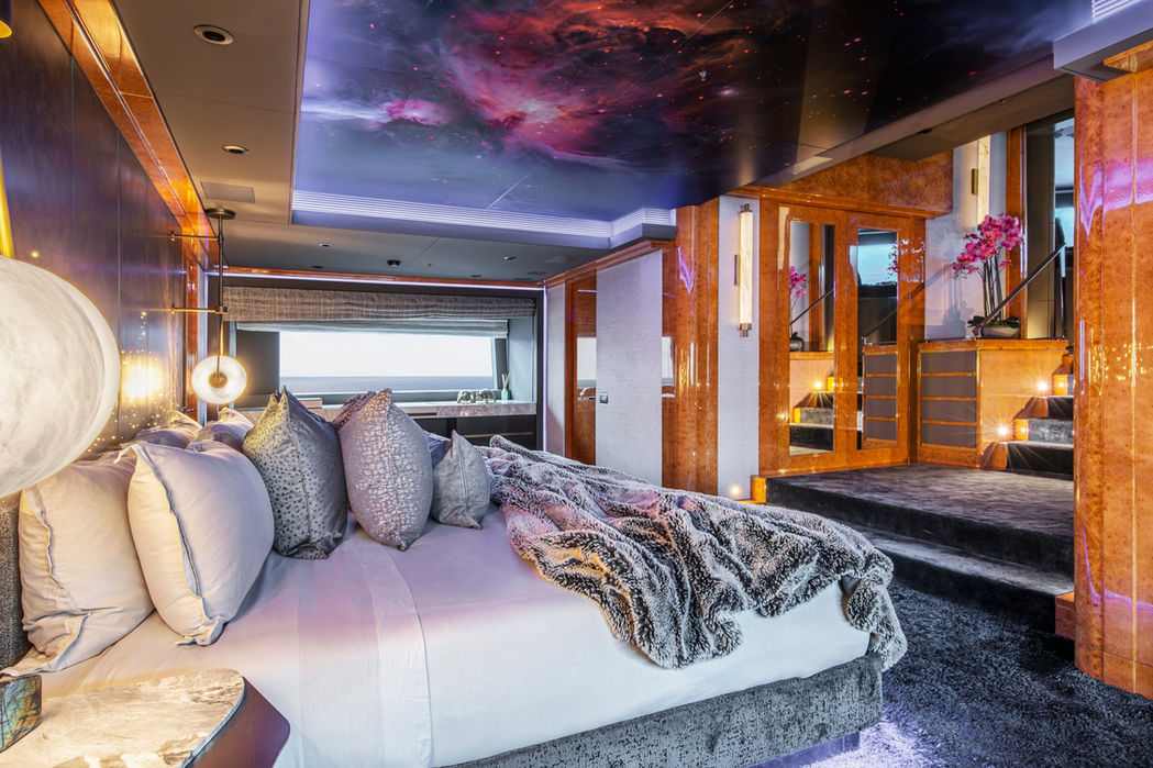 Master cabin on the Galaxy yacht with a large bed, warm lighting, and luxurious wood detailing.