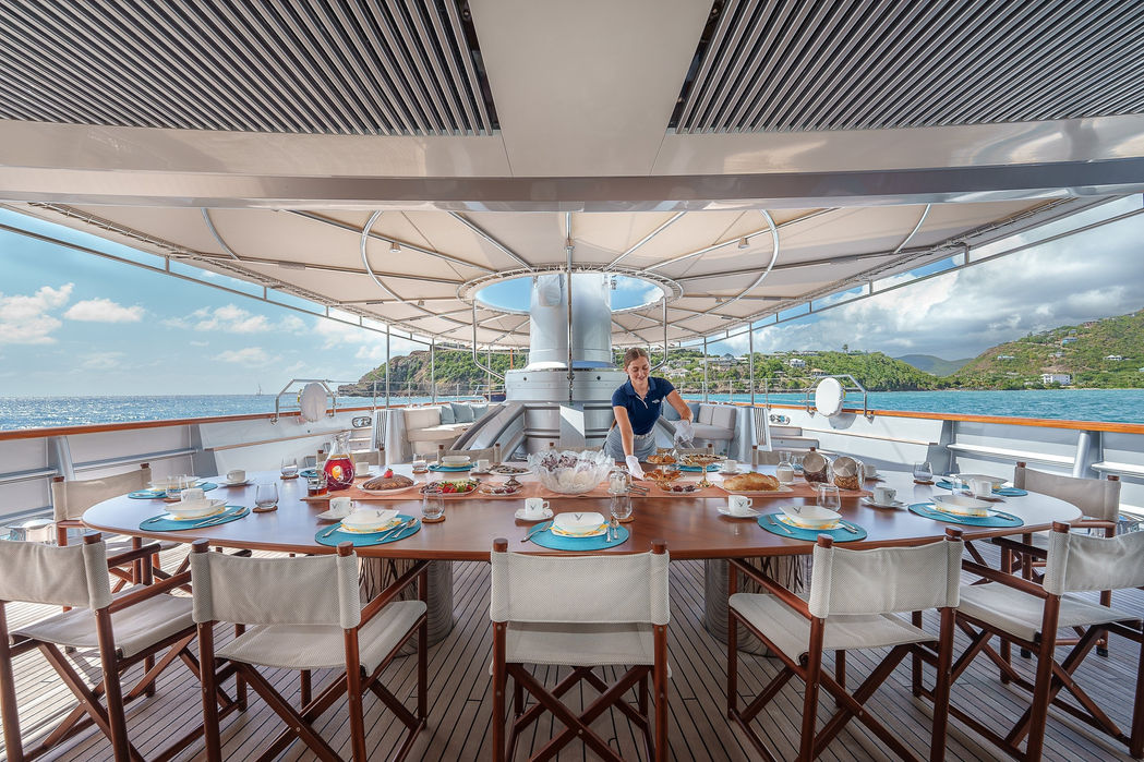 Aft deck dining layout aboard a sailing superyacht with ocean backdrop.