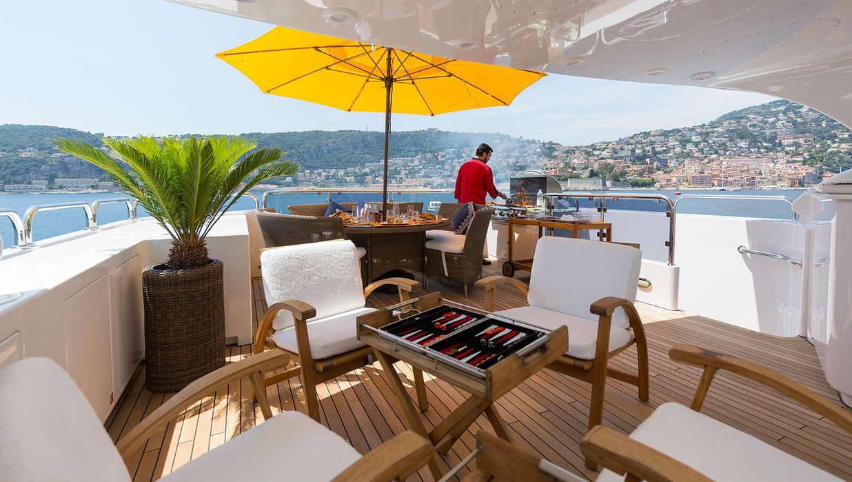 Shaded sun deck on M/Y Bina featuring lounge furniture and coastal views