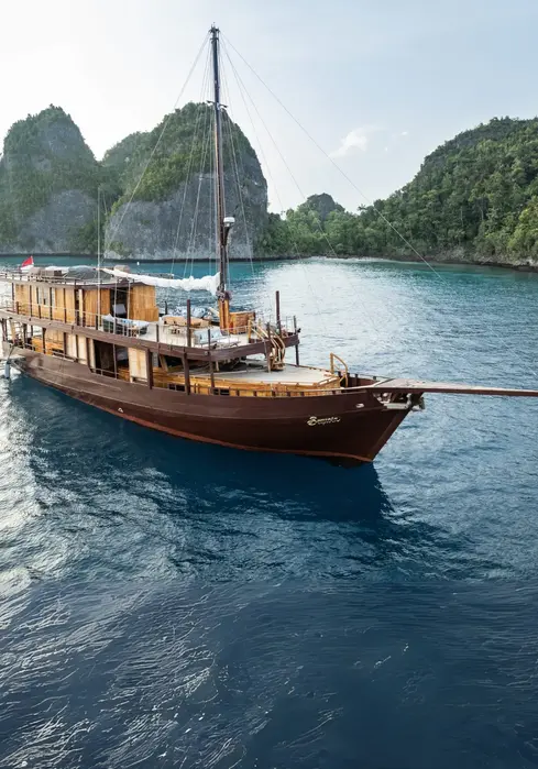 Side profile of Mahodaya Phinisi cruising in Komodo waters on a private charter with Navélia Yacht Charters Indonesia.