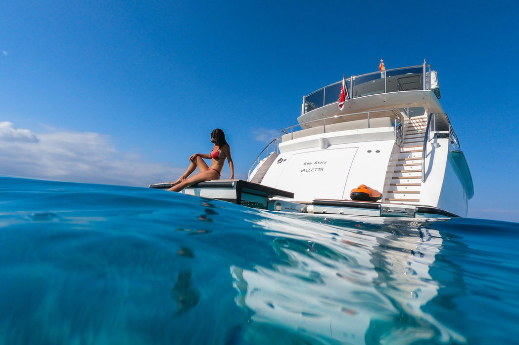 Guest using the swim ladder of Sea Story yacht in clear Mediterranean water