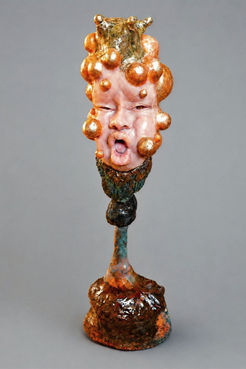 Glänzende skulpturale Büste mit rosigem Gesicht, goldenen kugelartigen Formen am Kopf und geöffnetem Mund auf langem schmalen Hals mit organischem Sockel.