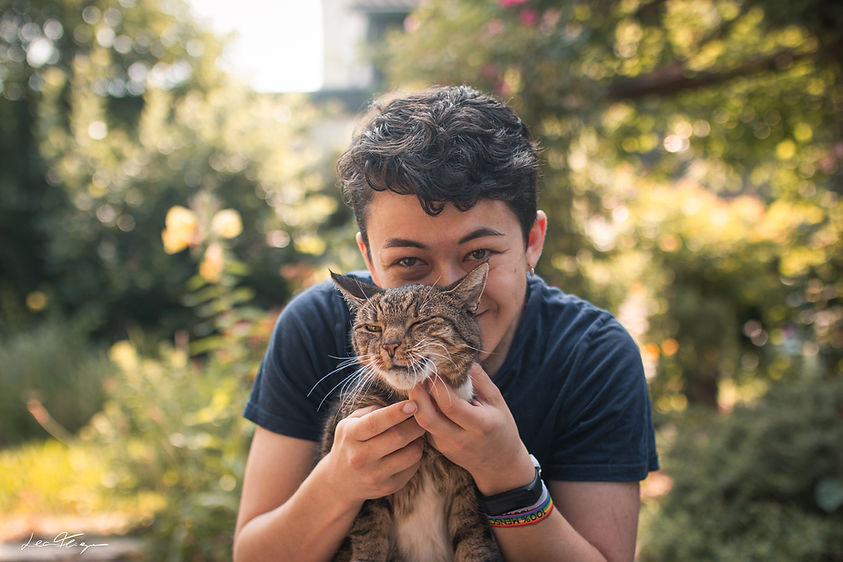 Portrait von mir und meiner Katze Diego auf meinem Schoร und in die Kamera grinsen. Der Hintergrund ist verschwommen mit verschiedenen Grรผntรถnen, da das Foto im Garten gemacht wurde.