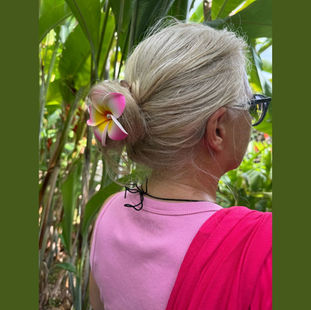 eine blonde Frau mit Hibiskus-Blüte im Haar mitten in Palmen