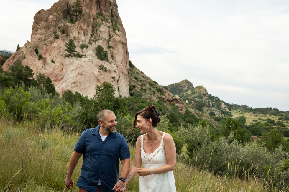 Couple strolling hand in hand through the lush green fields beneath the red sandstone formations.