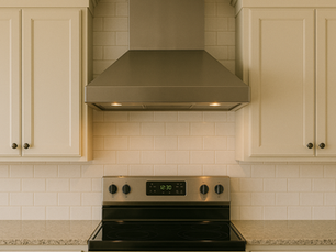 Stainless steel stove with hood, flanked by white cabinets on a tiled backsplash. Oven display shows 12:30. Warm lighting creates a cozy mood.
