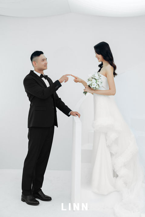 新人於棚內階梯對望，食指輕觸的細膩互動。 / Couple touching fingers on studio stairs, romantic Korean style interaction.