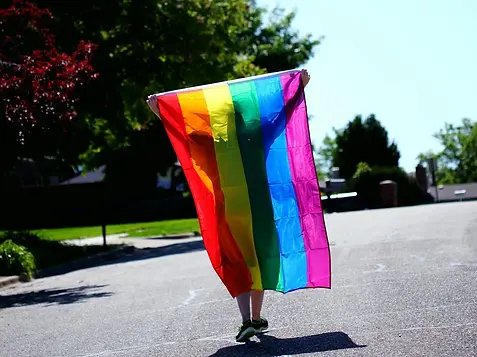 person walking down street holding up rainbow flag