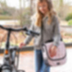 Rosa Fahrrad-Tasche mit schwarzen Punkten wird von einem Maedchen getragen, sie steht neben einem Fahrrad