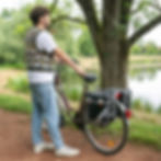 Doppeltasche Kunstleder 25l Retro, schwarz mit weißen Akzenten, auf dem Gepäckträger am Fahrrad, ein Mann steht daneben