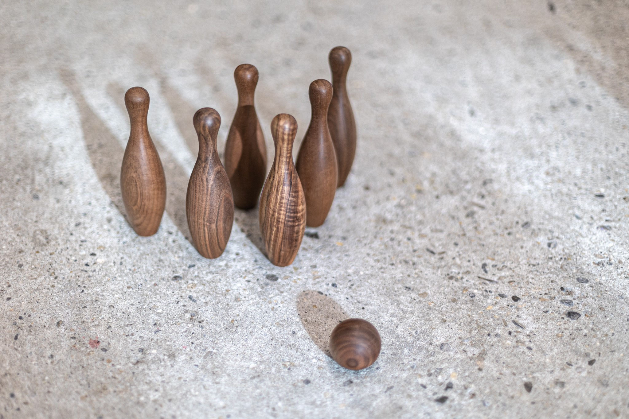 Sechs kunstvoll aufgereihte Kegel aus geöltem Nussbaumholz mit individueller Maserung, vor denen eine handgefertigte Holzkuge
