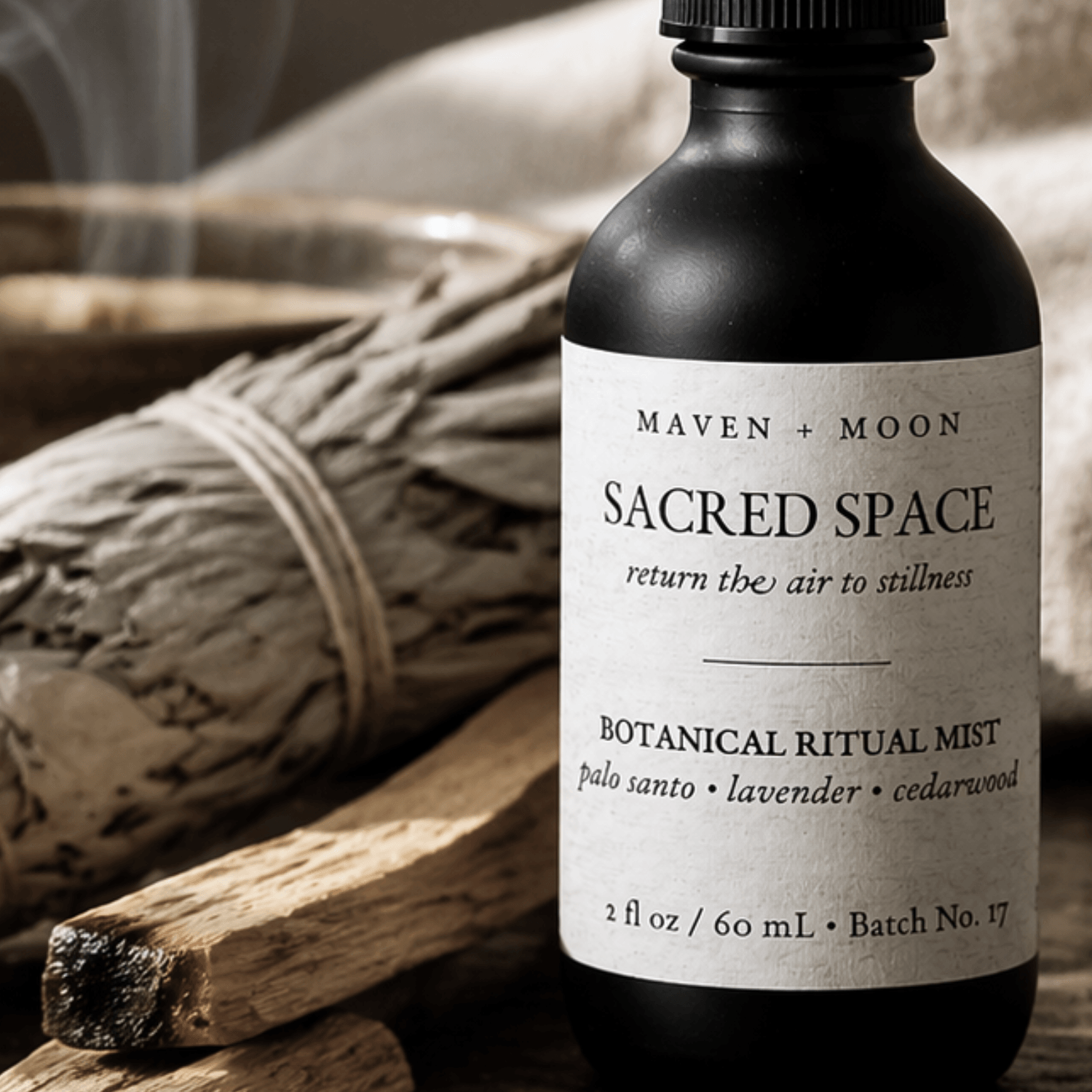 black matte spray bottle with editorial modern apothecary label sitting next a white sage bundle, palo santo stick, and clear