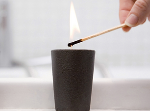 Long match lighting a candle in a black matte candle tumbler.