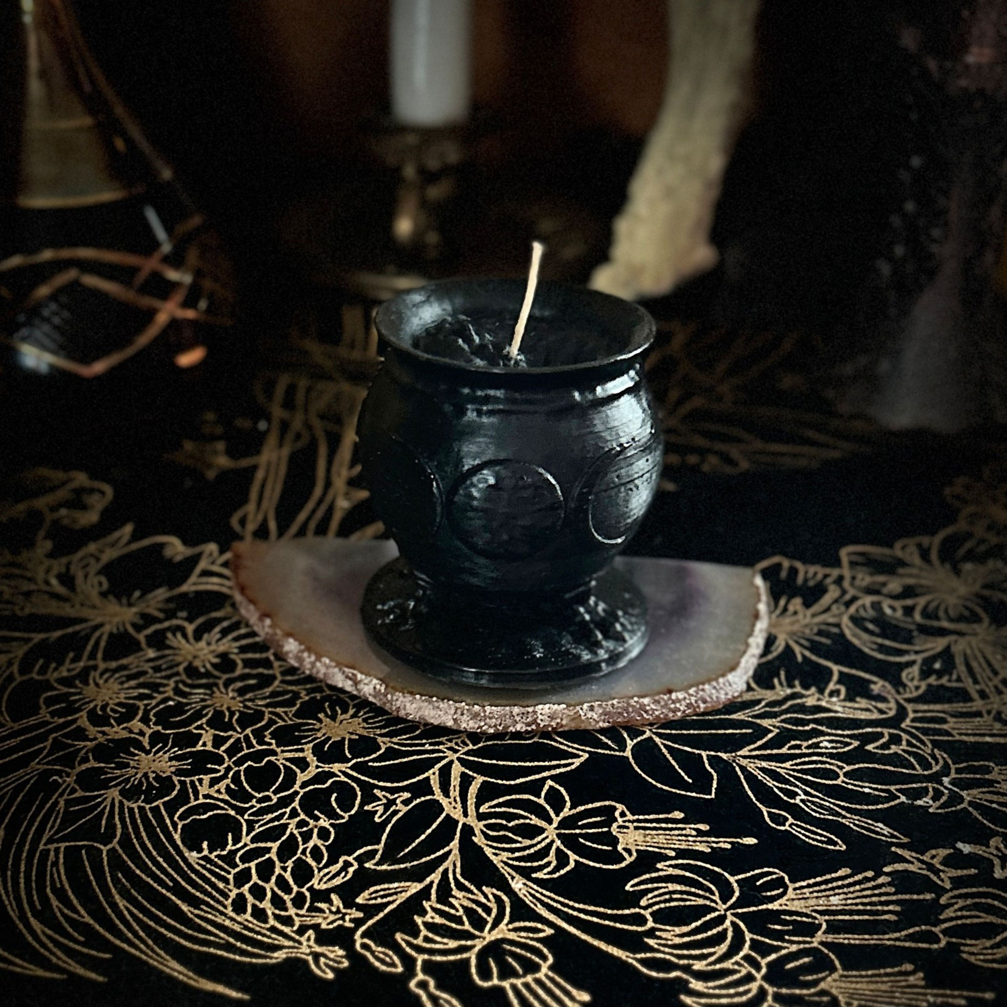 Beeswax black triple moon cauldron candle sits atop an agate stone on an altar