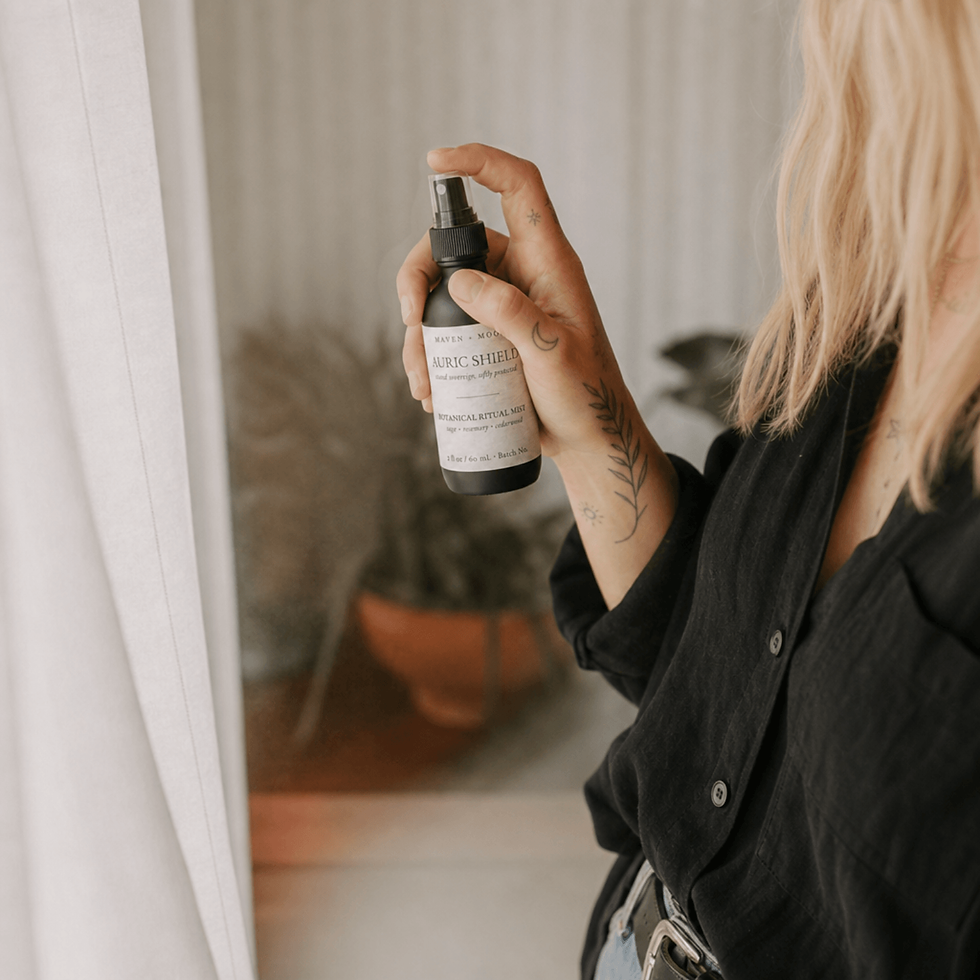 Thumbnail: Person holding Auric Shield botanical ritual mist beside a softly lit window while wearing a black linen shirt in a calm atmo