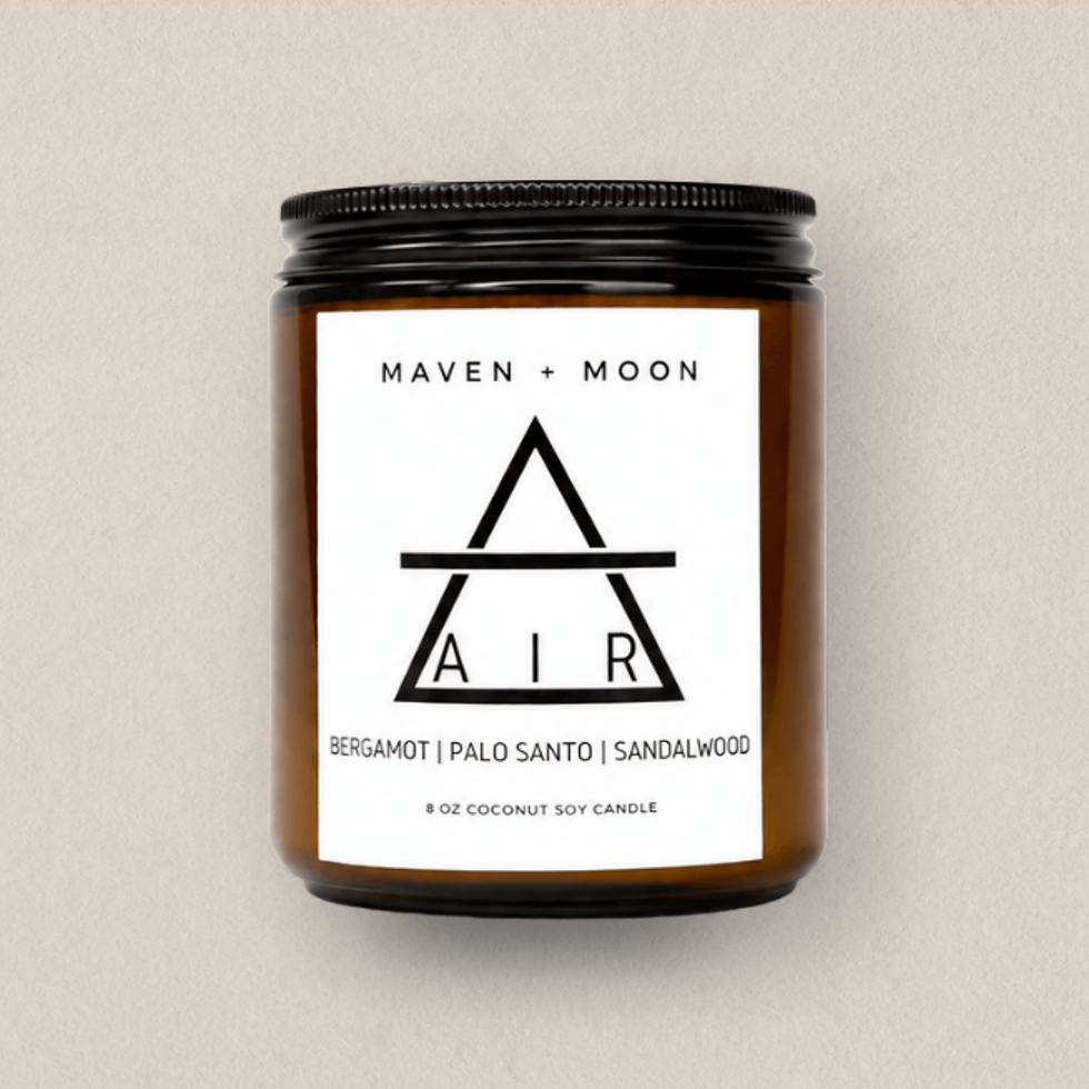 Air Element soy candle in an amber glass jar with balck screw top lid, photographed against a soft parchment-toned background