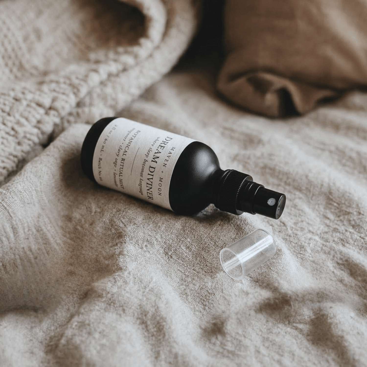 Dream Diviner ritual mist bottle laying on textured linen with cap removed, relaxed natural setting, warm soft lighting
