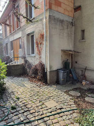 Façade arrière de la maison existante avant rénovation, montrant la connexion en cours avec l'extension en construction.