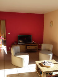 Ancien salon avant rénovation avec mur rouge, TV et mobilier en bois.