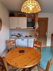 Ancien coin repas avec mobilier rustique et petite cuisine dans un appartement à rénover en station de montagne.