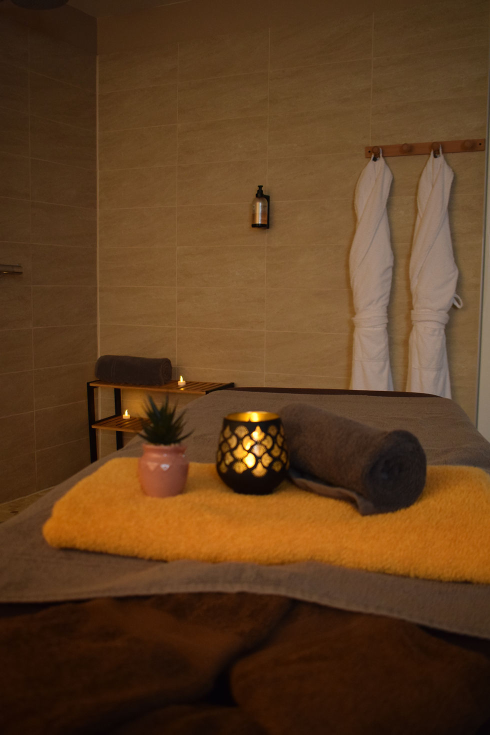 Salle de massage spa aux tons beige, serviettes blanches, bougies allumées et ambiance calme.