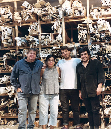 Four people standing together in a workshop filled with shelves of wooden frame materials and tools