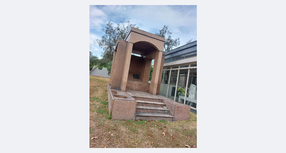 Stone structure with steps in grassy area. The Heritage Park in background.