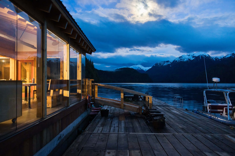 Evening shot of Khutzeymateen Wilderness Lodge glowing warmly under the evening sky, surrounded by lush wilderness.