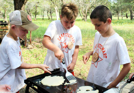 Three boys, outdoors cooking on a grill