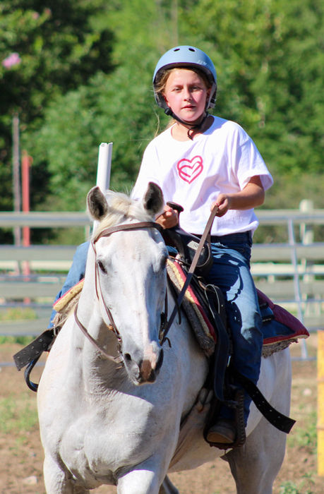 Girl riding a white horse that is trotting.
