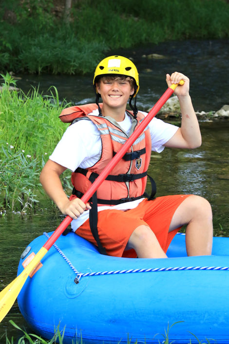 Boy sitting in an inflatable kayak on the river, holding an oar