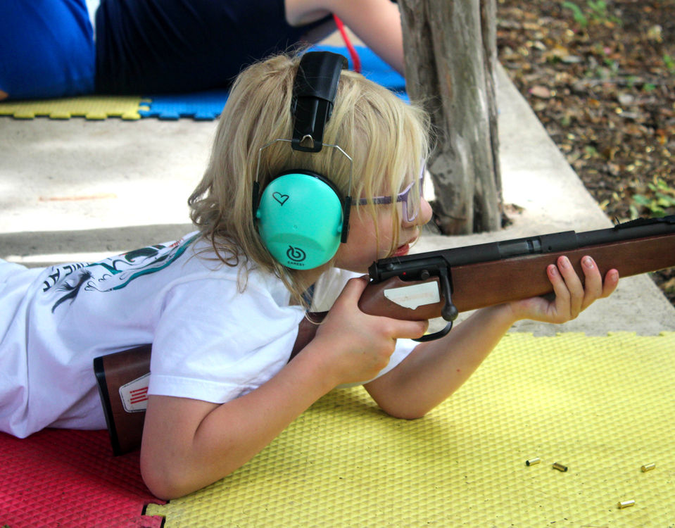 A young girl wearing ear protectors aiming a rifle.