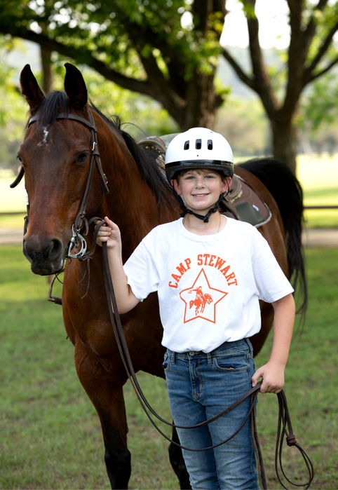 A boy wearing a Camp Stewart t-shirt wearing a helmet, in front of his horse