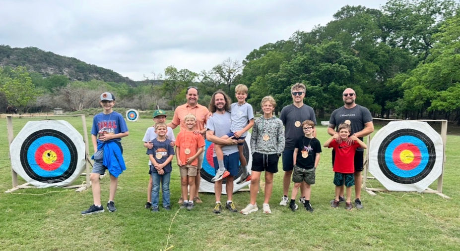 Group of fathers and sons standing in a field with archery targets