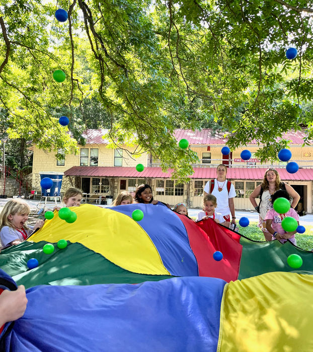 Group of young girls surrounding and holding up a colorful tarp upon which bright green and blue balls are bouncing.
