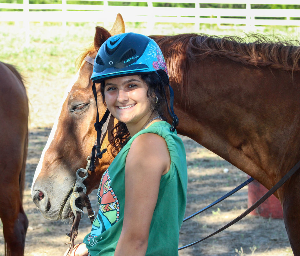 Girl in a green shirt and riding helmet walking with a brown horse.