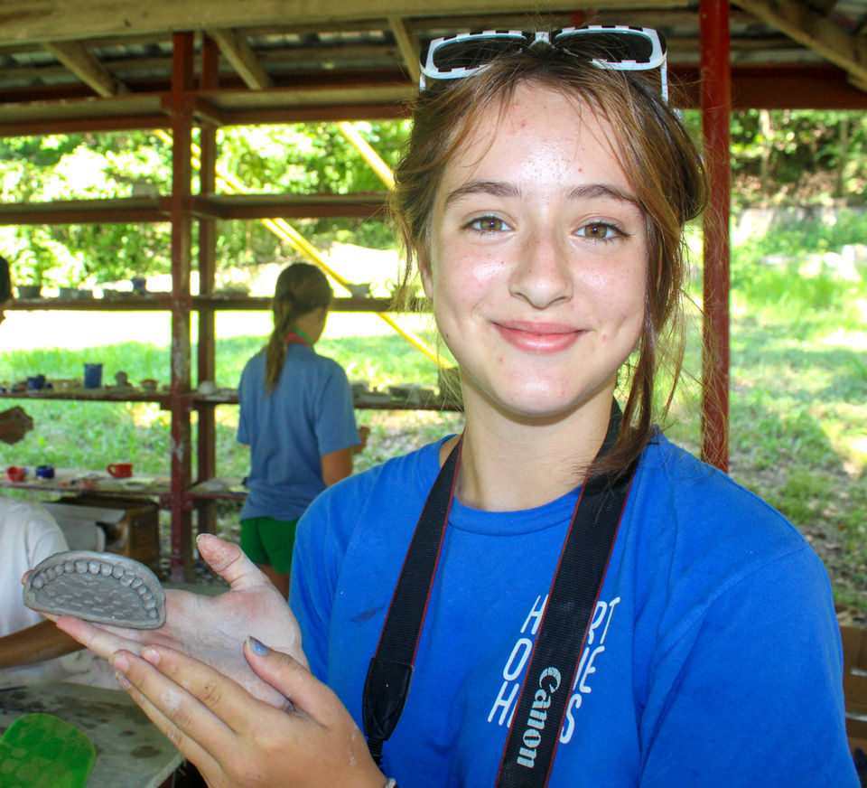 Girl working with clay who is looking at the camera, smiling.