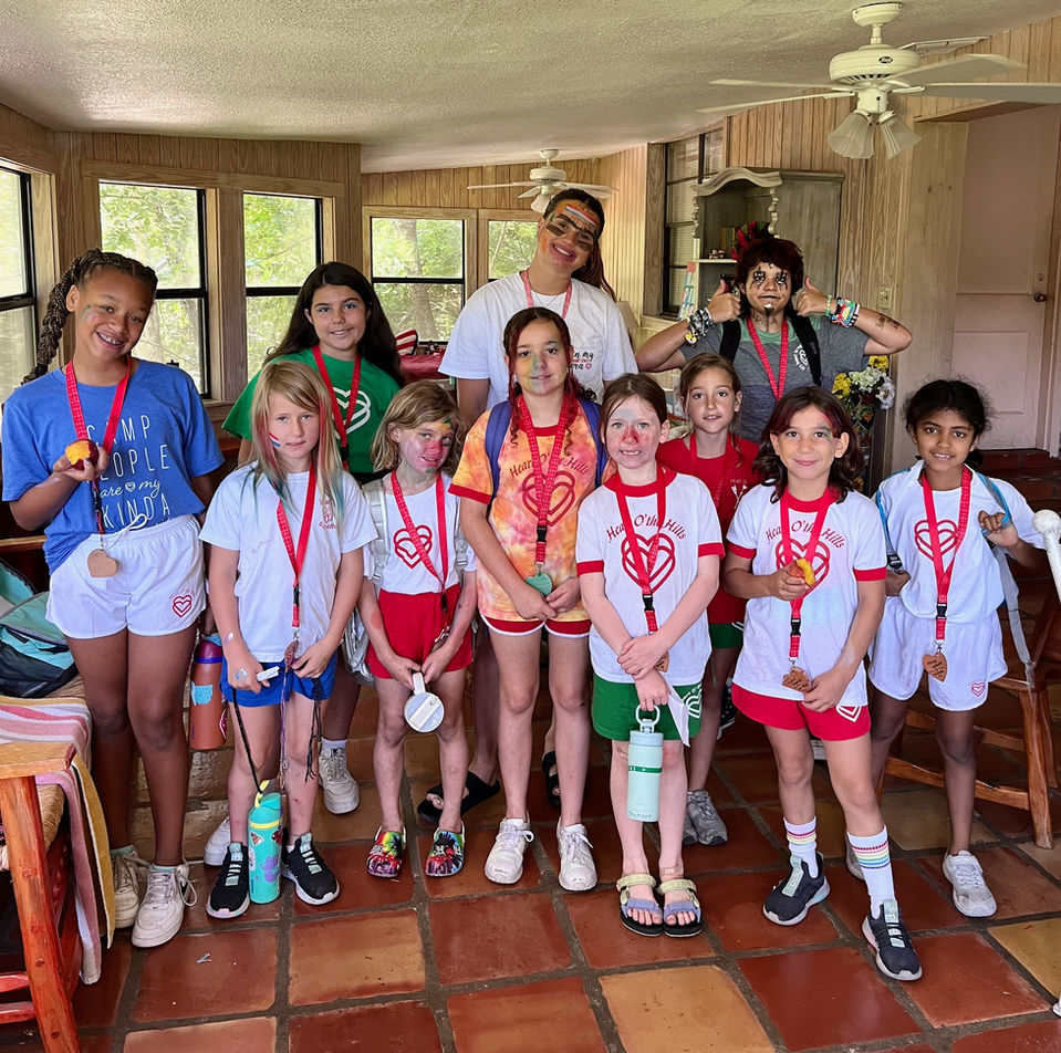 Seven young girls wearing Heart O' the Hills t-shirts and lanyards with 4 older girl counselors or counselors in training.