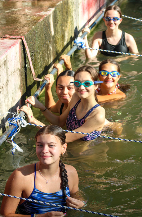 Group of 5 girls in bathing suits at the finish line of a swimming exercise.