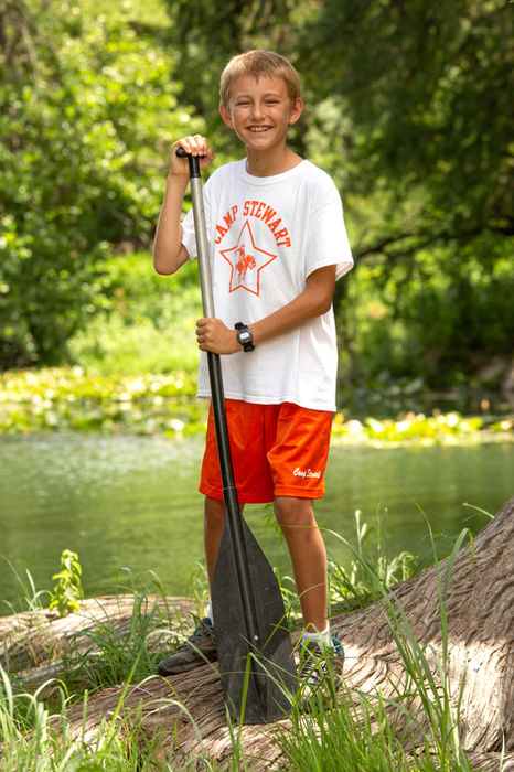 Boy wearing a Camp Stewart uniform standing in next to the river, holding an oar