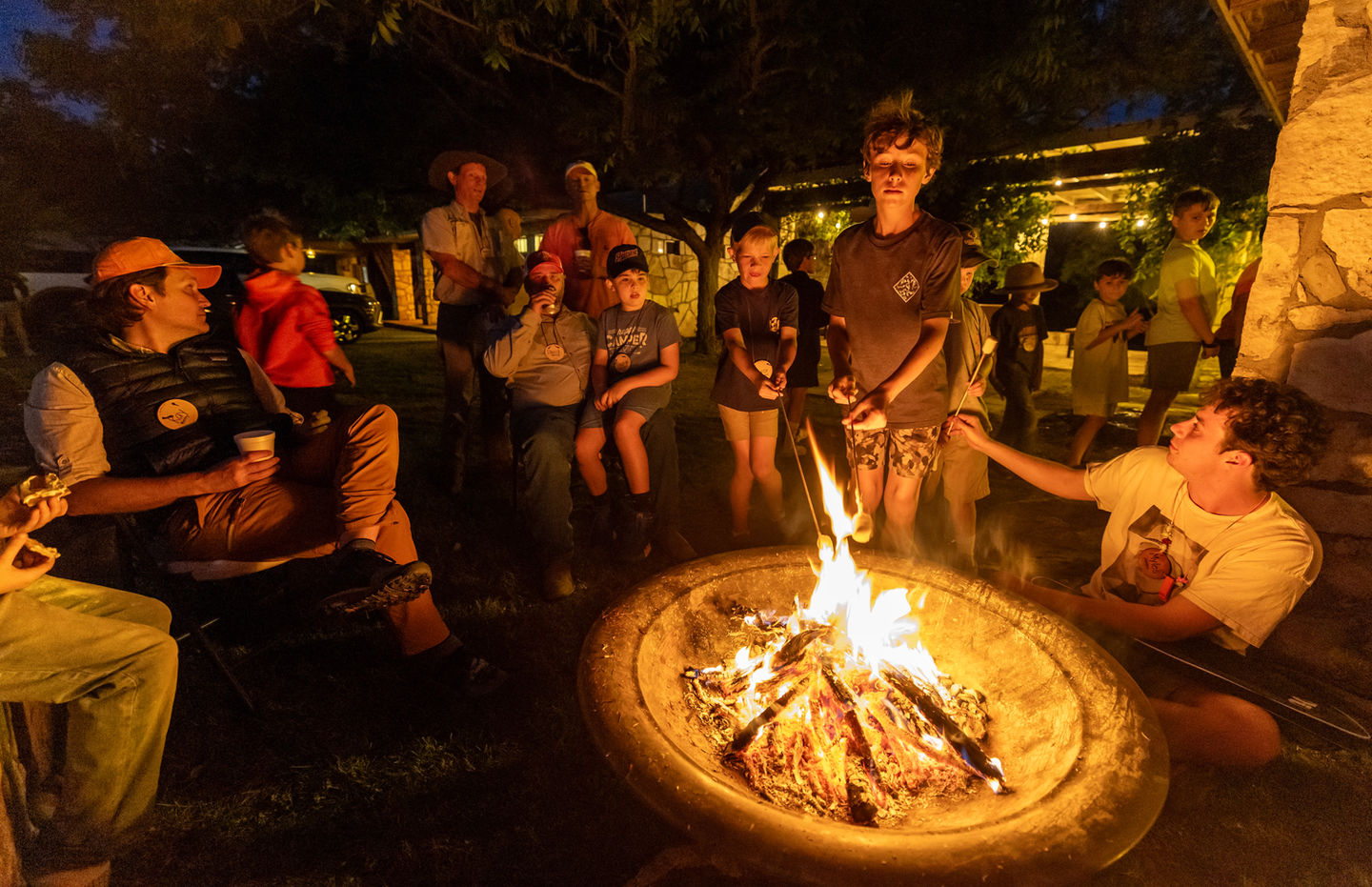 Group of fathers and sons sitting outdoors at night around a camp fire