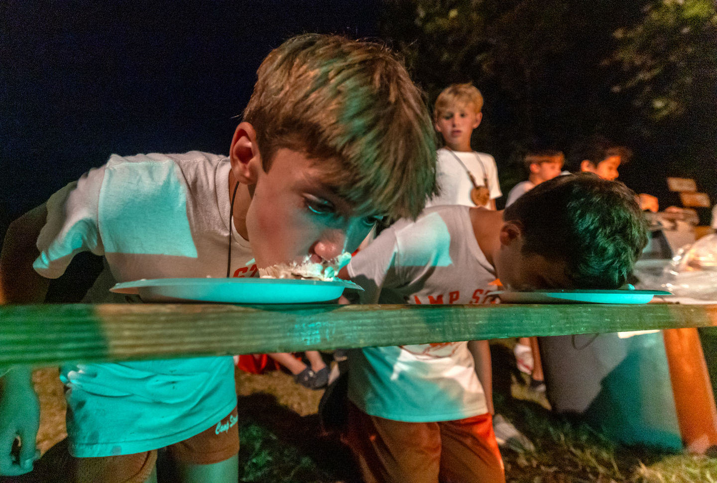 Two boys with their heads down in plates participating in a pie eating contest