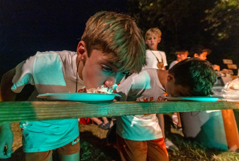 Two boys with their heads down in plates participating in a pie eating contest